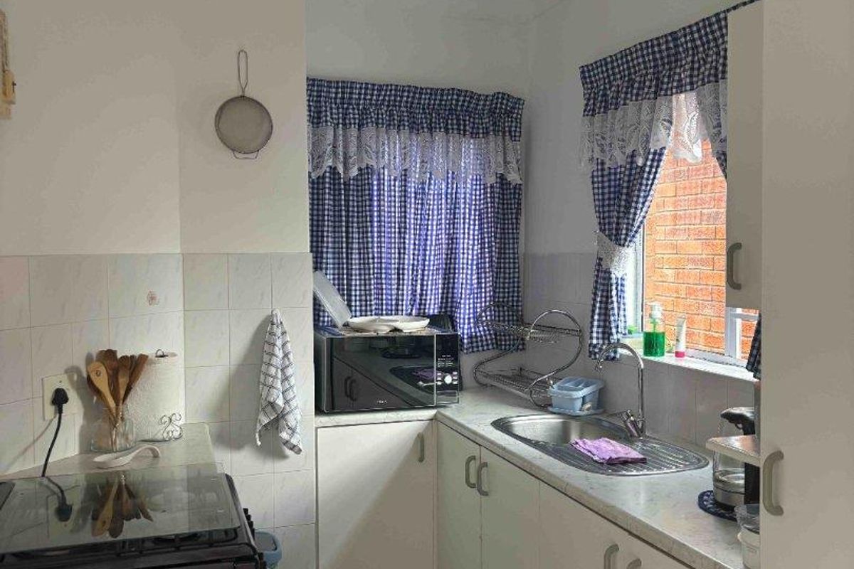 A functional kitchen featuring white cabinetry, laminate countertops, a stainless steel sink, and tiled flooring, offering a practical layout for daily meal preparation.