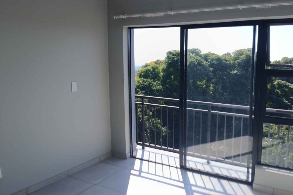 An empty bedroom featuring tiled flooring and a sliding glass door that opens onto a balcony with a scenic tree-lined view.