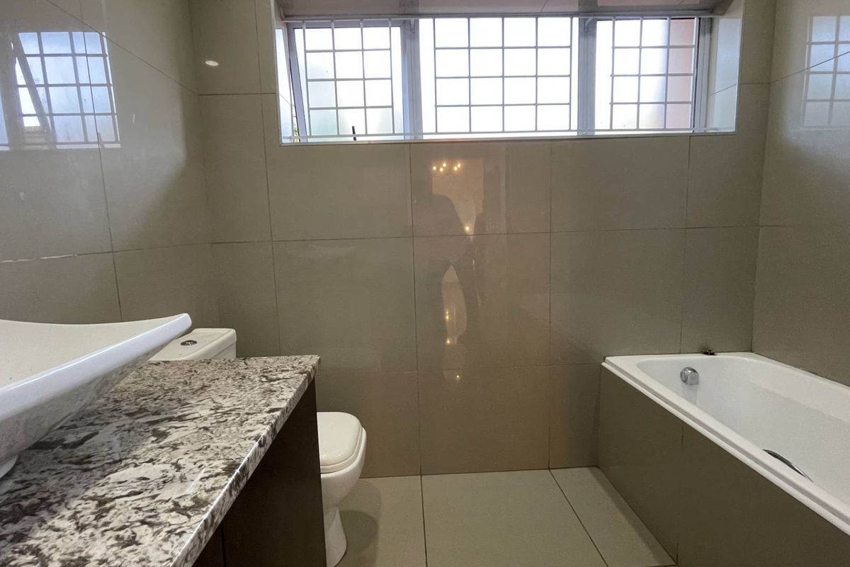 A functional bathroom featuring a vessel sink on a granite vanity, a bathtub, and neutral wall-to-floor tiling with security bars on the window.