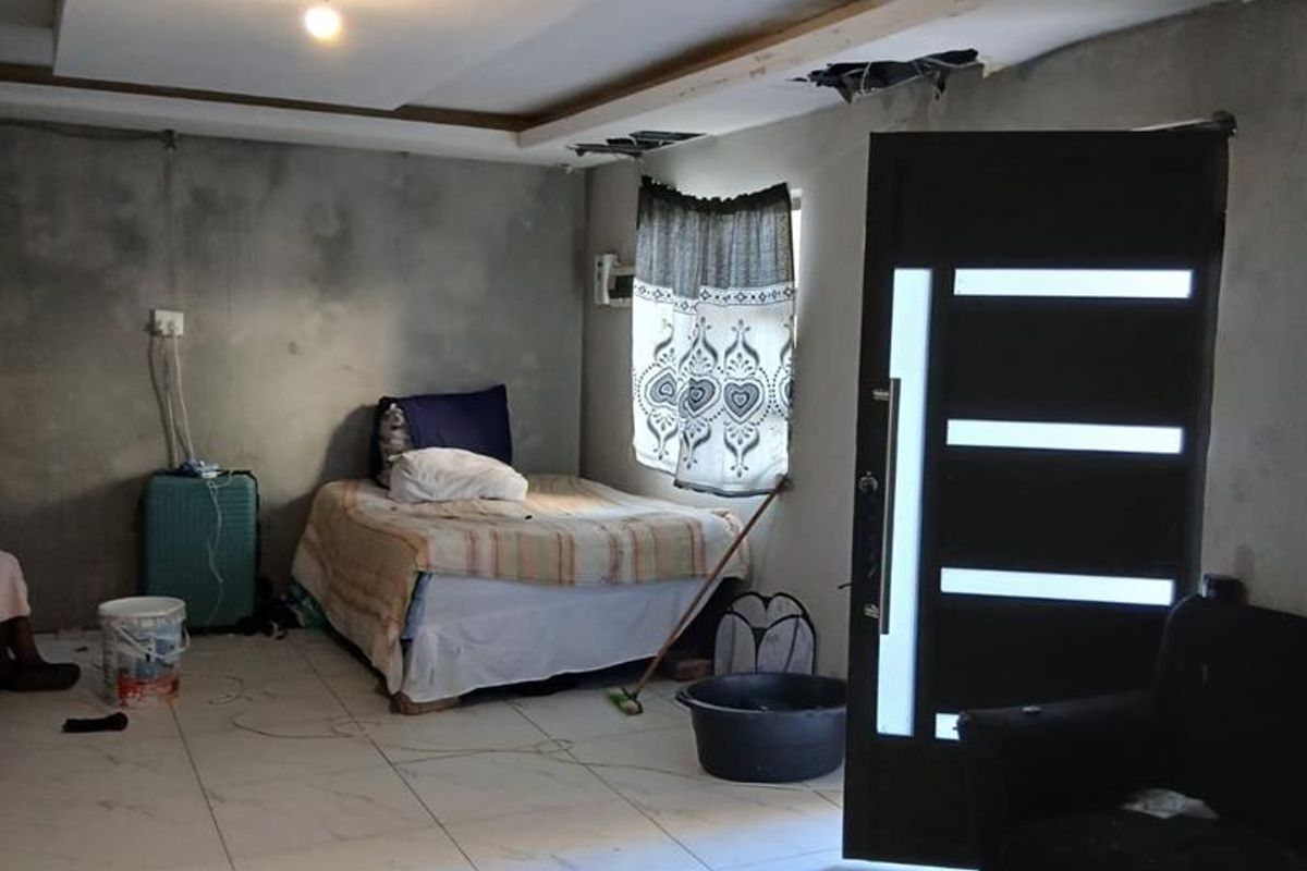 A bedroom space featuring tiled flooring and an unfinished ceiling, currently undergoing renovation with exposed structural elements.