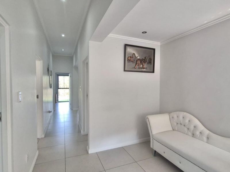 A bright, neutral hallway featuring tiled flooring and recessed downlighting, providing access to adjacent rooms including a bathroom with a glass shower enclosure.