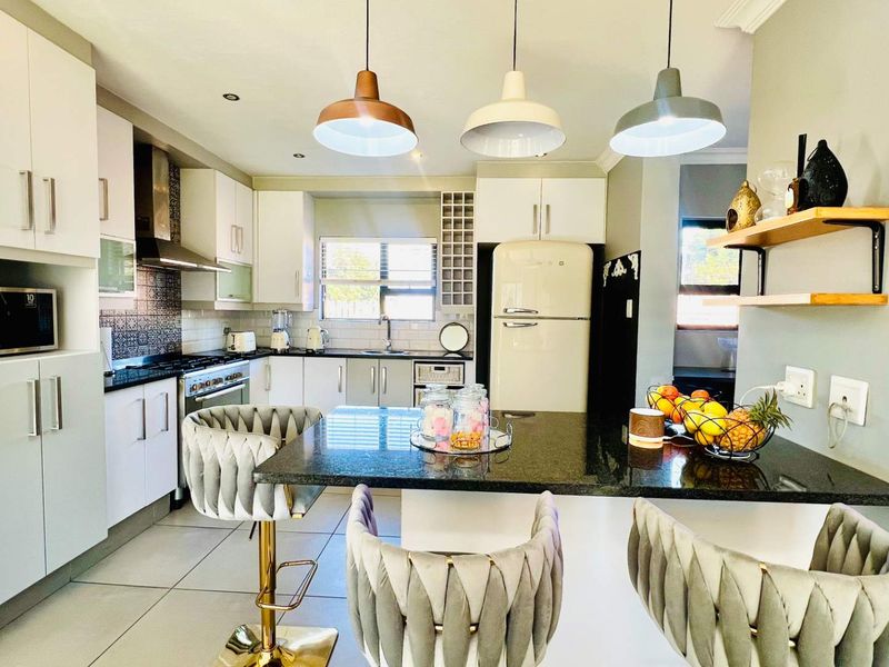 Modern kitchen featuring white cabinetry, granite countertops, a gas stove, and a central breakfast island with pendant lighting.