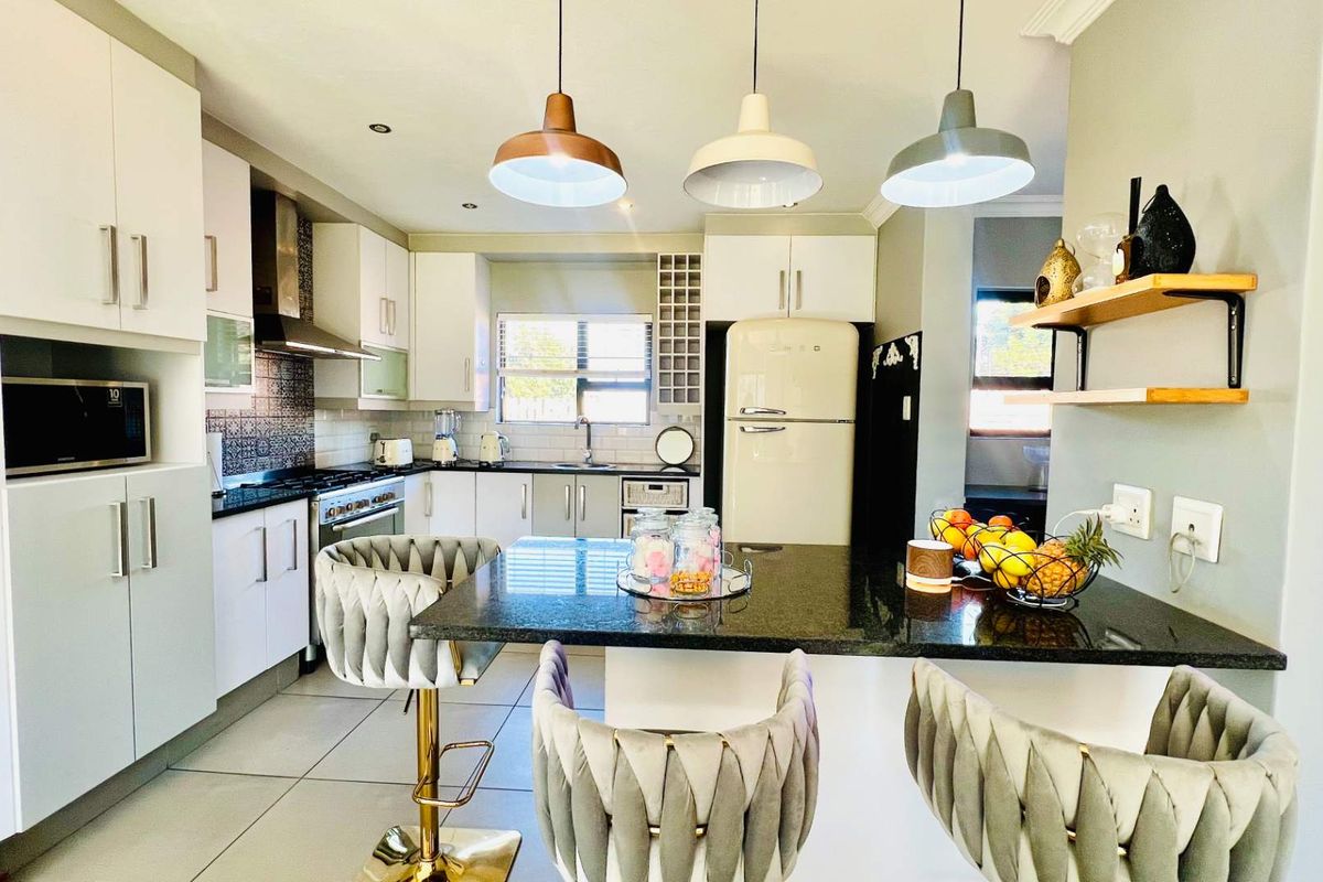 Modern kitchen featuring white cabinetry, granite countertops, a gas stove, and a central breakfast island with pendant lighting.
