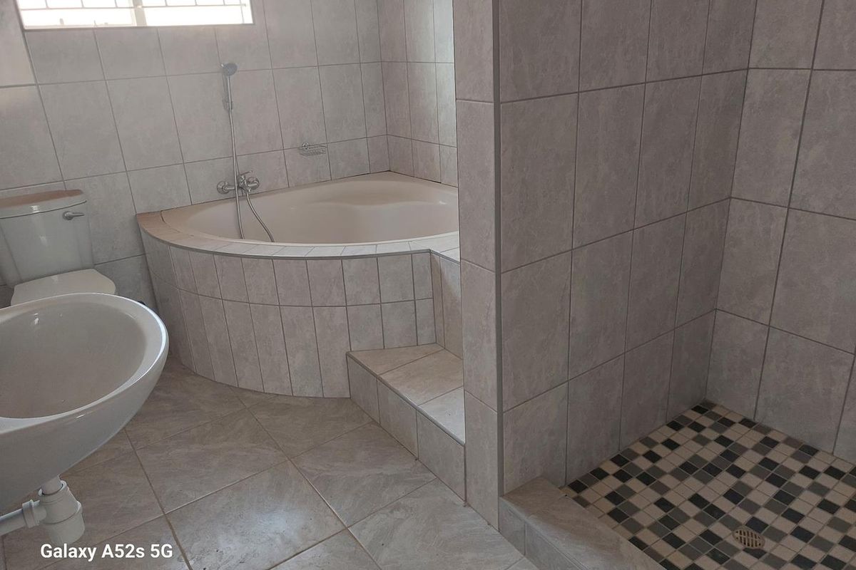 A functional bathroom featuring a corner bathtub, a separate walk-in shower with mosaic floor tiling, and neutral wall tiles.