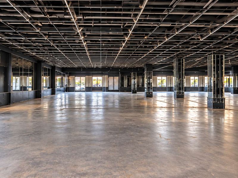 Expansive open-plan commercial space featuring polished concrete floors, exposed grid ceiling, and mirrored structural columns, offering a versatile layout for various business uses.