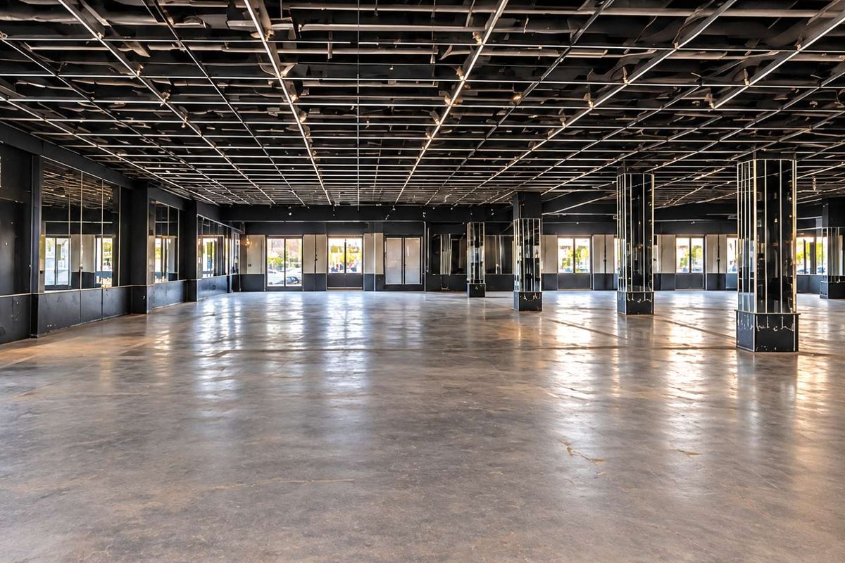 Expansive open-plan commercial space featuring polished concrete floors, exposed grid ceiling, and mirrored structural columns, offering a versatile layout for various business uses.