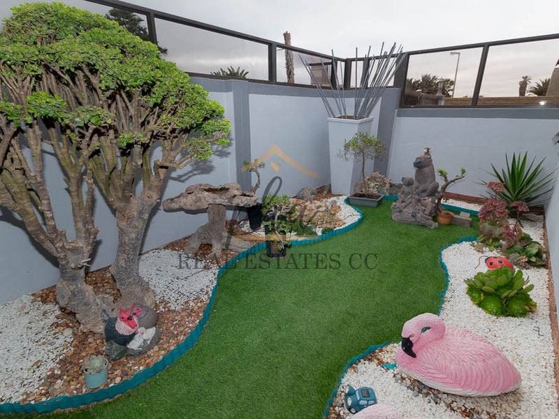 A compact, low-maintenance courtyard garden featuring artificial turf, decorative stone borders, and a modern glass balustrade boundary wall.