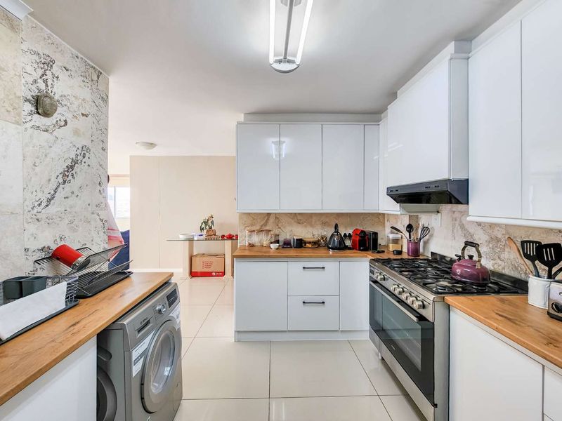 Modern kitchen featuring white cabinetry, wooden countertops, gas hob, oven, extractor fan, and stone tile backsplash with integrated laundry space.