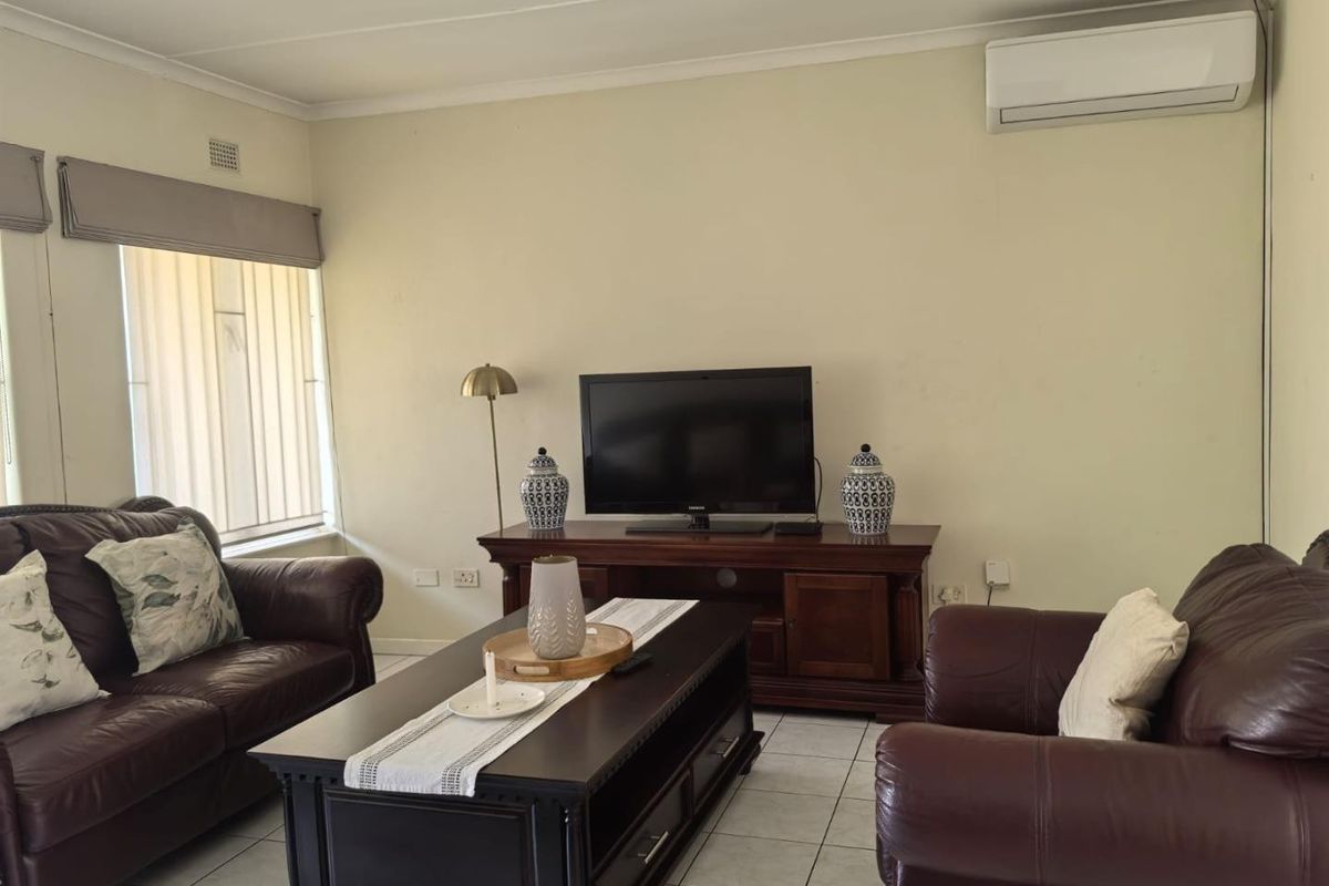 A comfortable living room featuring tiled flooring, a wall-mounted split-system air conditioner, and vertical window blinds.