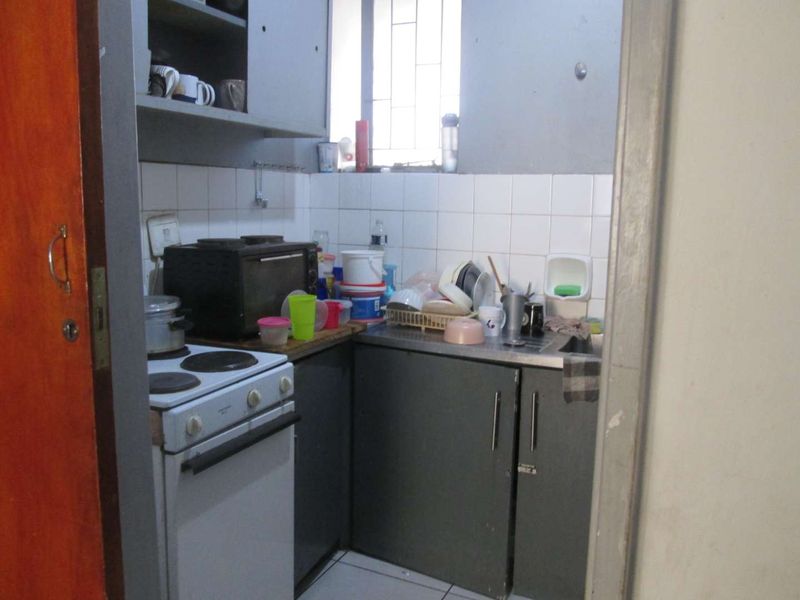A compact, dated kitchen featuring basic cabinetry, a tiled backsplash, and an electric stove, requiring modernization to improve functionality and aesthetic appeal.