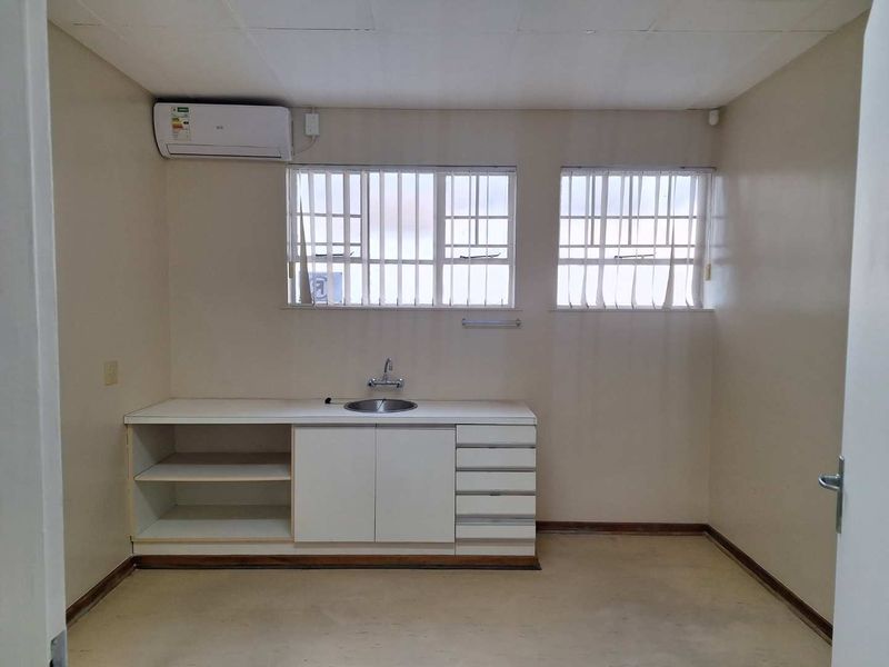 A functional office kitchenette featuring built-in cabinetry, a stainless steel sink, and a wall-mounted air conditioning unit.
