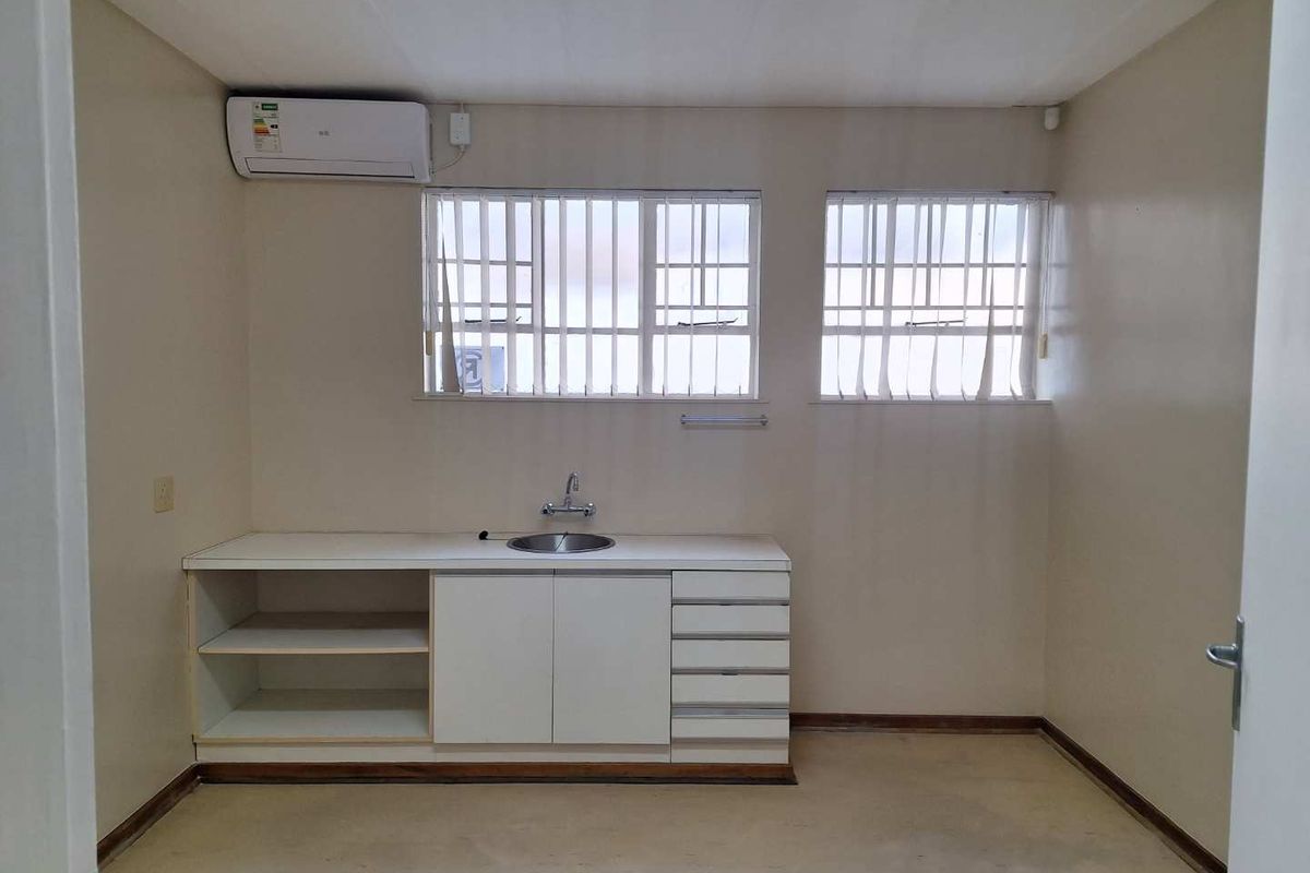 A functional office kitchenette featuring built-in cabinetry, a stainless steel sink, and a wall-mounted air conditioning unit.