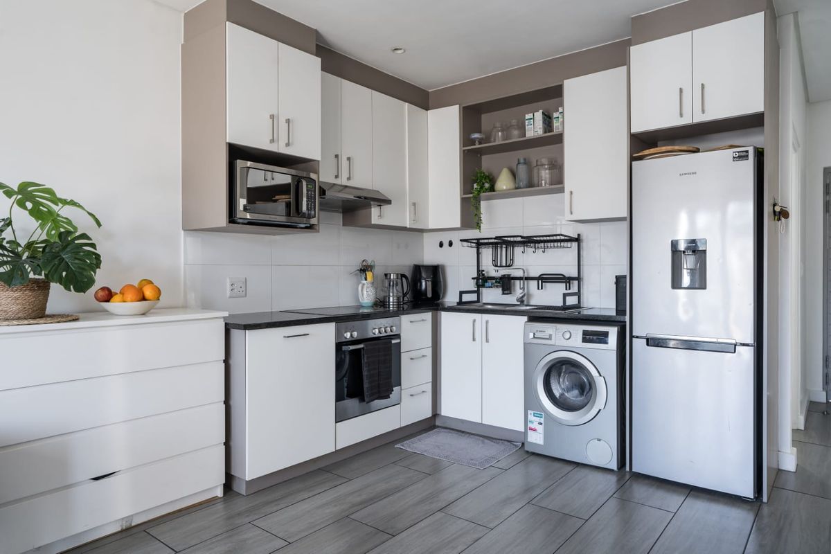 Modern kitchen featuring white cabinetry, dark laminate countertops, built-in oven, hob, extractor fan, and integrated washing machine with sleek tiled flooring.