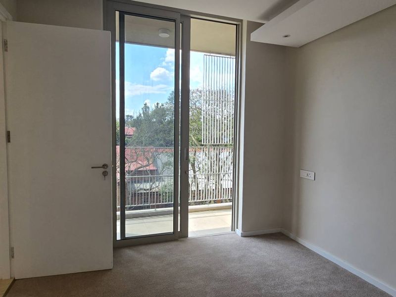 A bright, empty bedroom featuring neutral carpet flooring, a recessed ceiling detail, and a sliding glass door providing access to a private balcony.