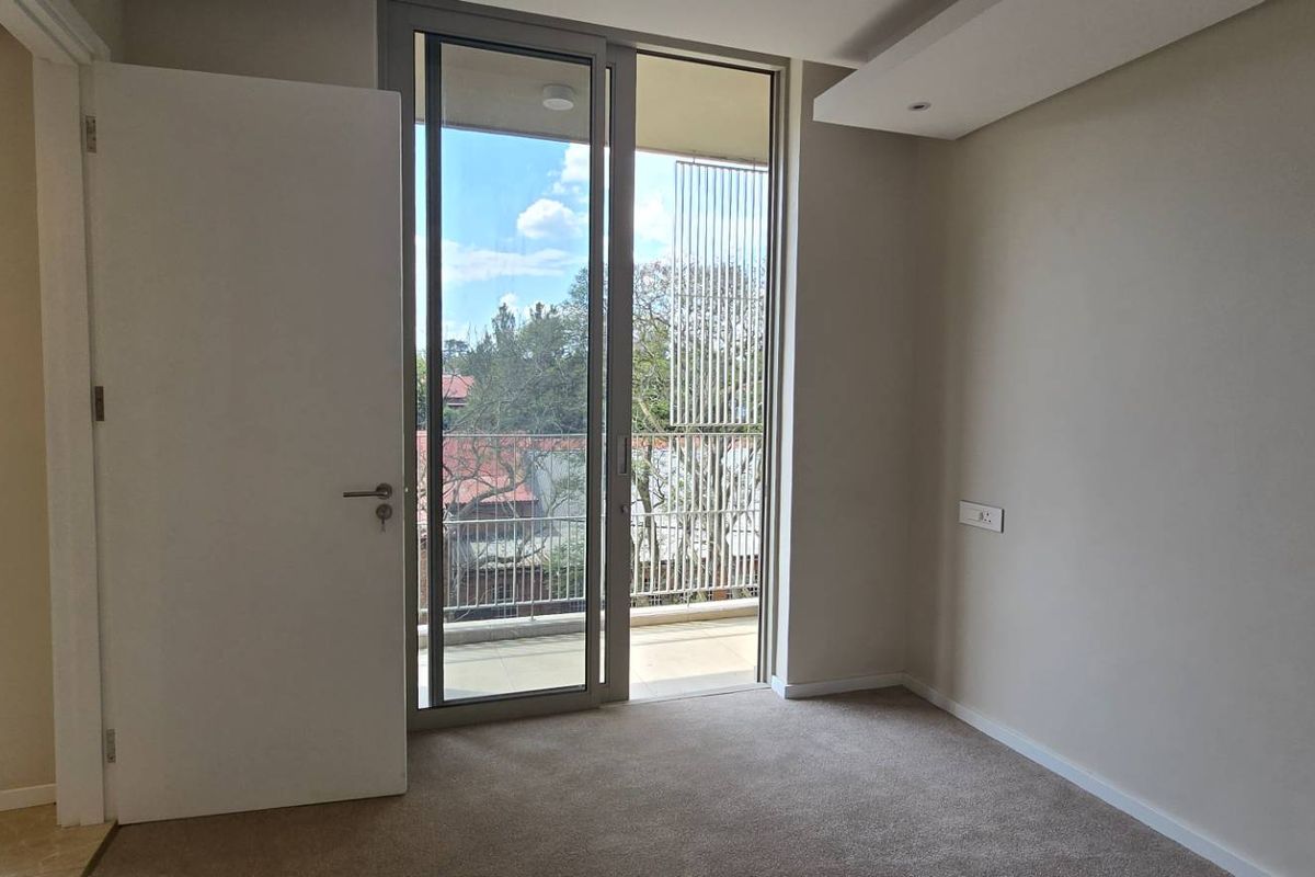 A bright, empty bedroom featuring neutral carpet flooring, a recessed ceiling detail, and a sliding glass door providing access to a private balcony.