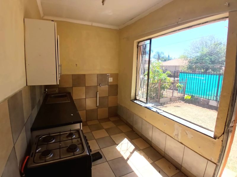 A compact kitchen featuring tiled flooring, a gas stove, and built-in cabinetry, with a large window providing natural light and garden views.