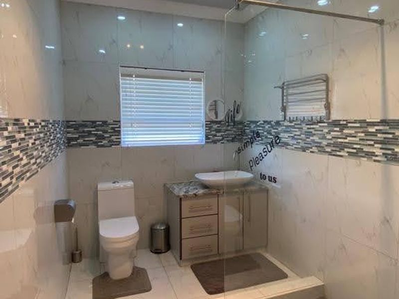 Modern bathroom featuring a glass-enclosed shower, vanity with vessel sink, toilet, and contemporary tiled finishes with a heated towel rail.
