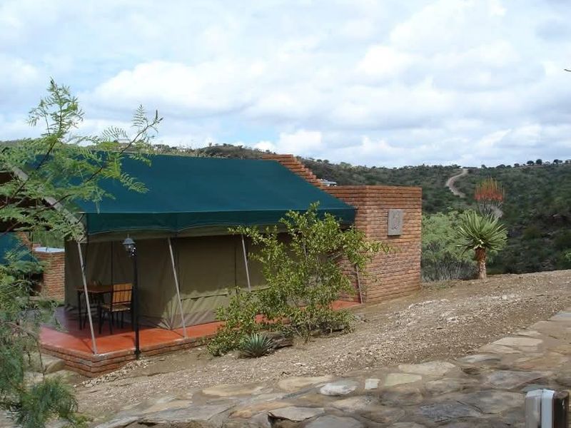 A lodge unit featuring a canvas tent structure with a brick wall extension, set on a tiled patio overlooking a natural landscape.