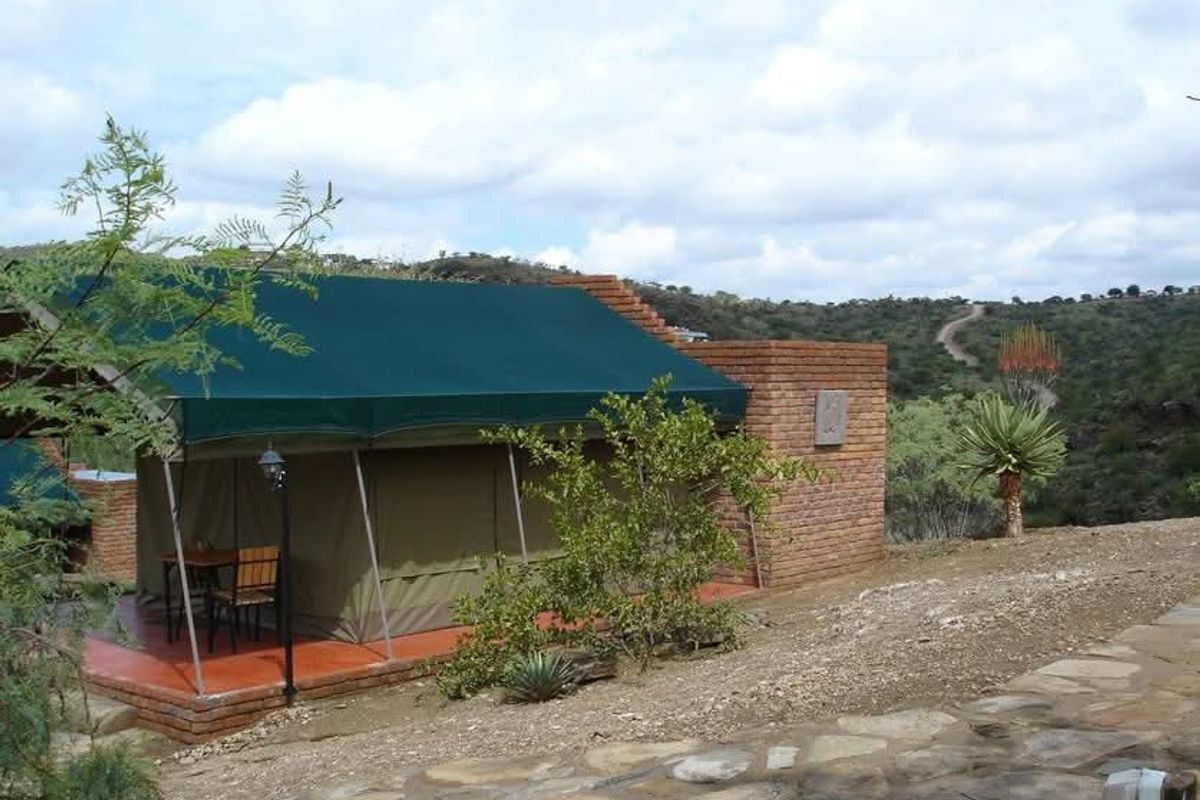 A lodge unit featuring a canvas tent structure with a brick wall extension, set on a tiled patio overlooking a natural landscape.