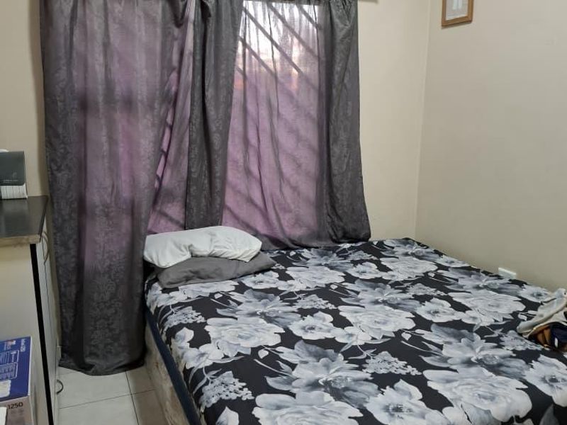 A functional bedroom featuring tiled flooring and window security bars, providing a basic and practical living space.