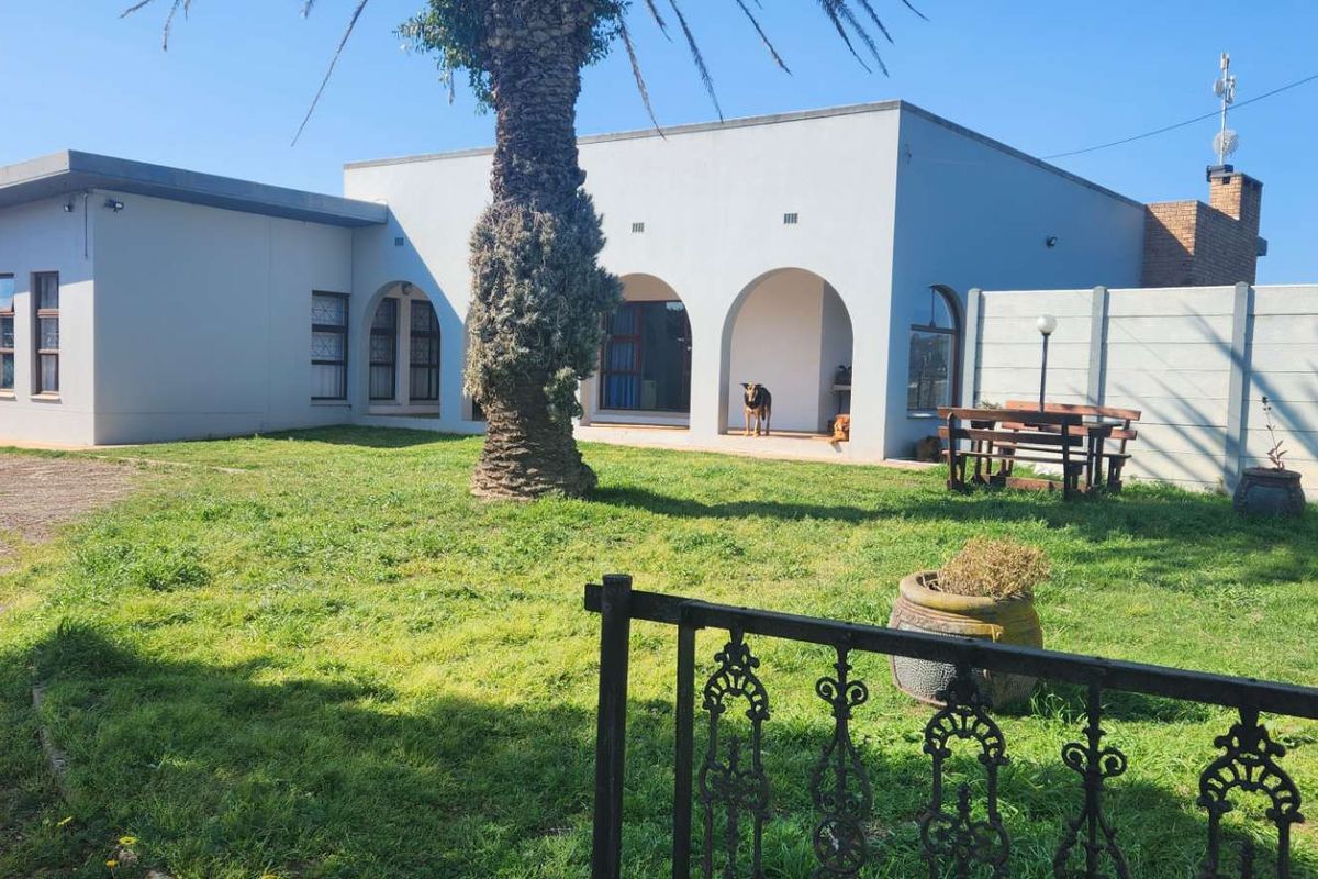 Rear view of the farm property featuring a lawn, arched veranda, and secure boundary walling.