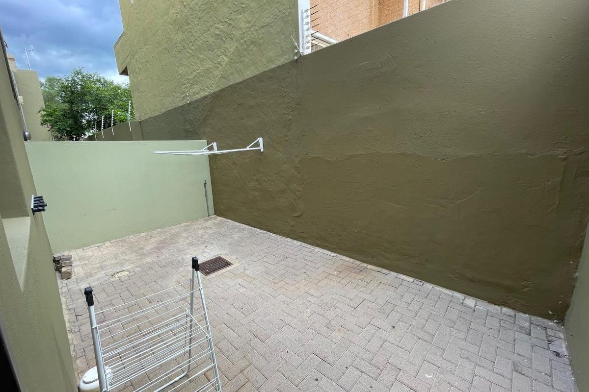 A paved rear courtyard area featuring high boundary walls, an integrated wall-mounted drying rack, and drainage infrastructure.