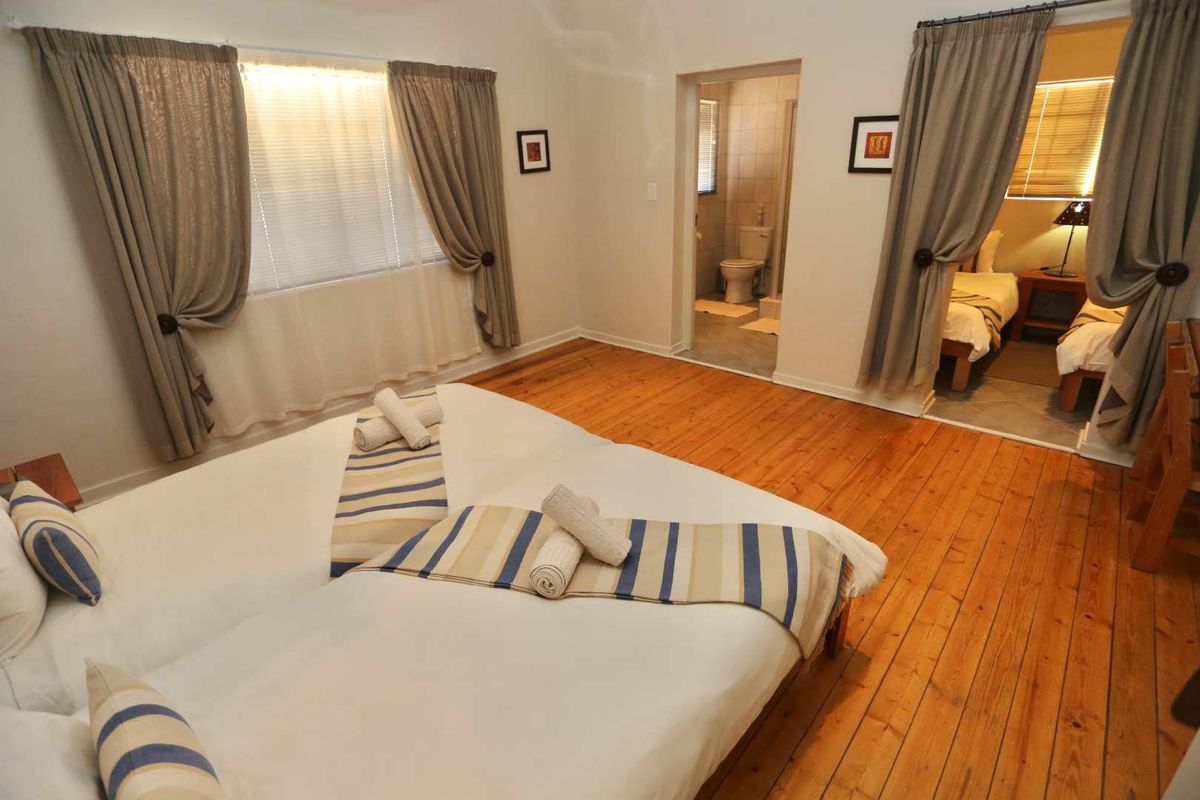 A hotel bedroom featuring polished timber flooring, an en-suite bathroom, and an adjoining room, offering a functional and classic layout.