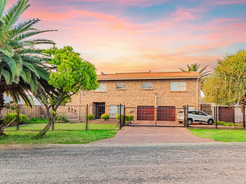 Front elevation of a double-story brick house featuring a paved driveway, double garage, and secure metal perimeter fencing.