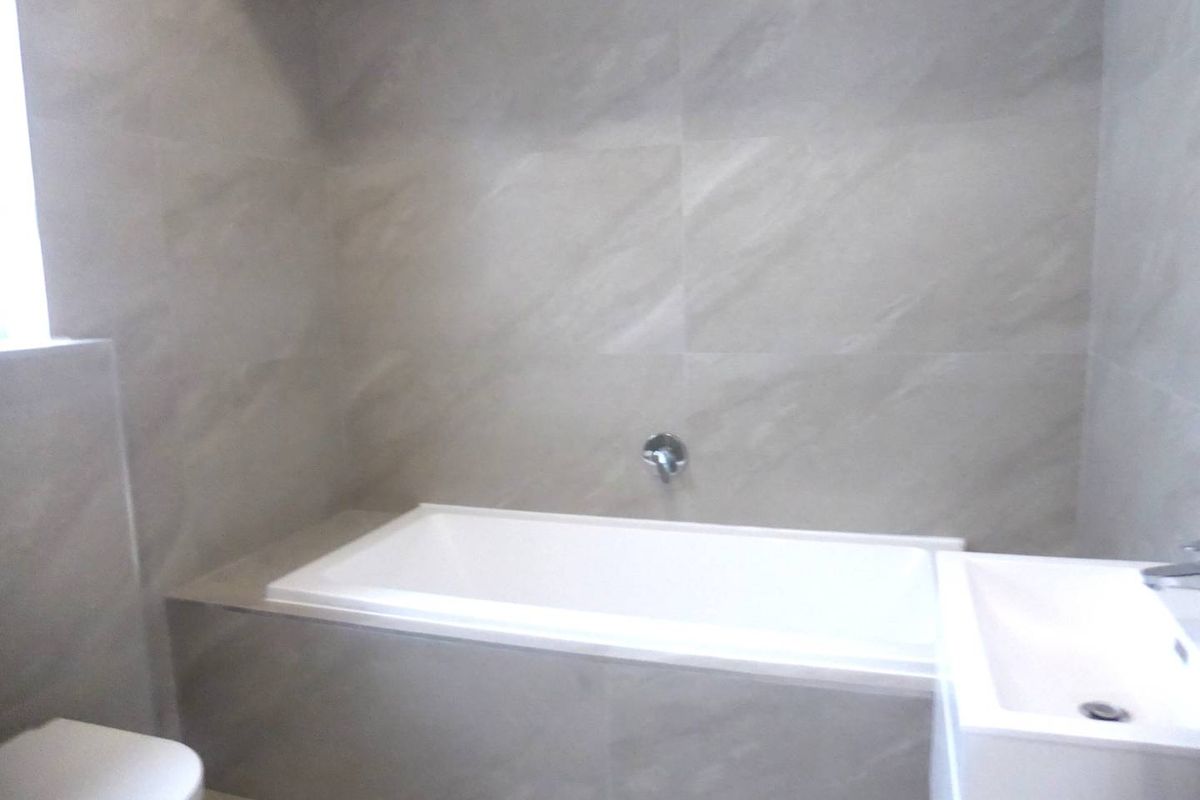 A modern bathroom featuring a built-in bathtub with wall-mounted fixtures, neutral wall tiling, and a clean vanity basin.