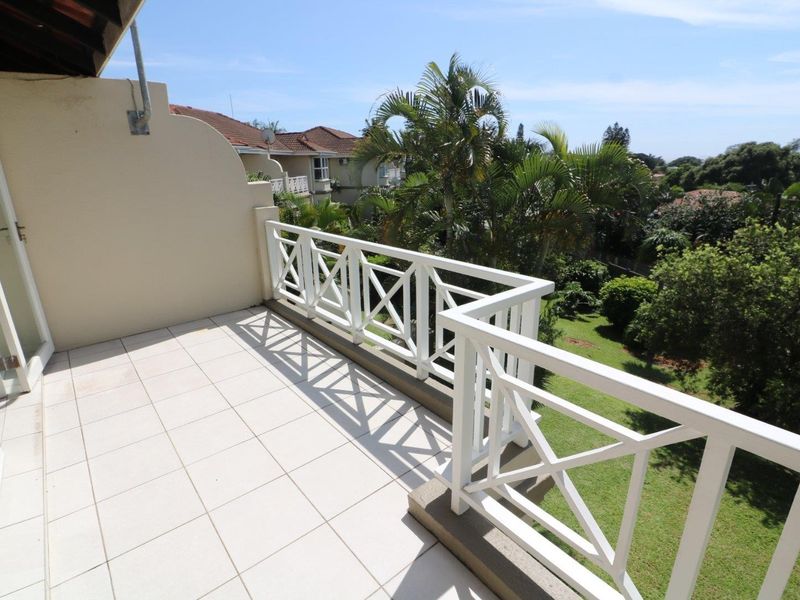 A spacious, tiled balcony featuring a decorative white balustrade and pleasant views over the surrounding garden and neighborhood.