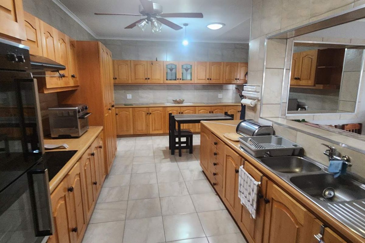 Spacious kitchen featuring extensive timber cabinetry, double stainless steel sink, built-in oven, and tiled flooring with a functional layout.