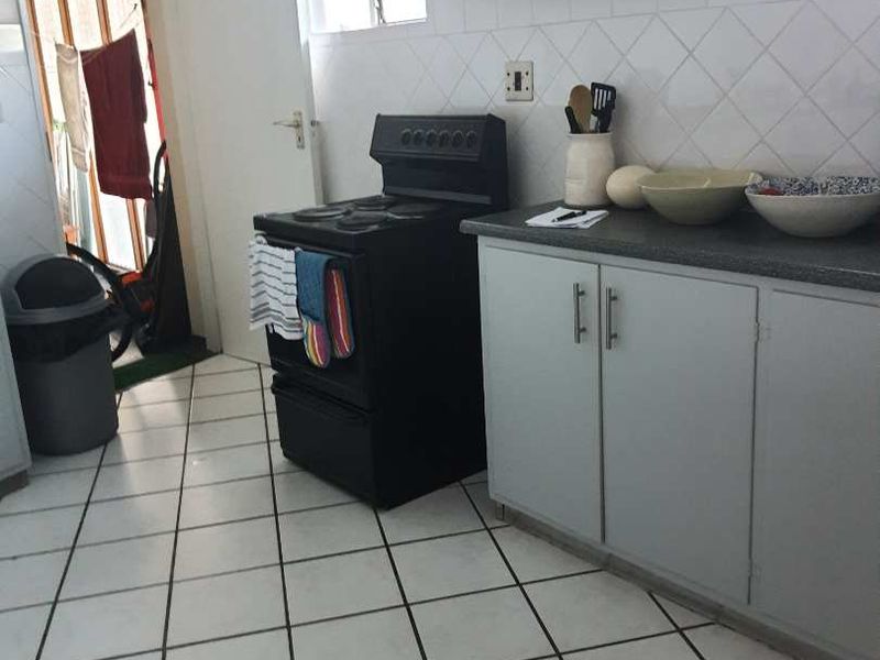 A functional kitchen featuring tiled flooring, built-in cabinetry with laminate countertops, a tiled backsplash, and a freestanding stove.