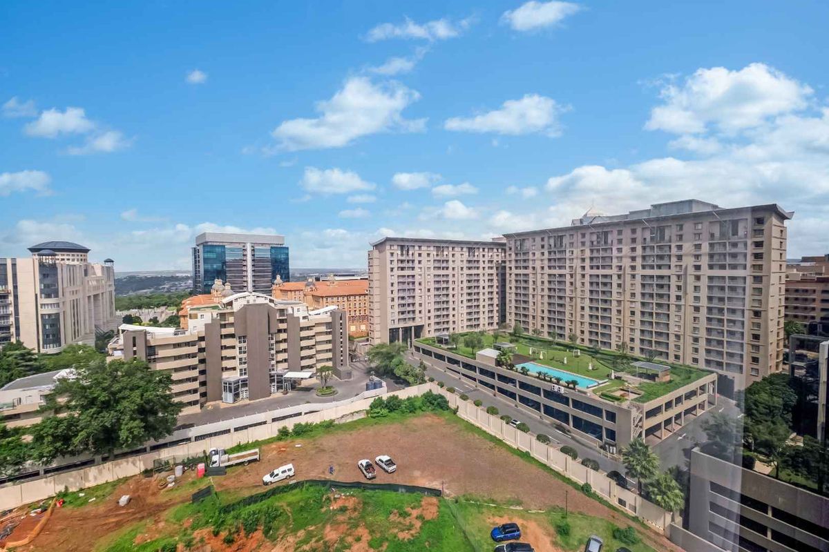 Elevated aerial view overlooking the surrounding urban landscape, featuring nearby apartment complexes and commercial buildings under a clear blue sky.