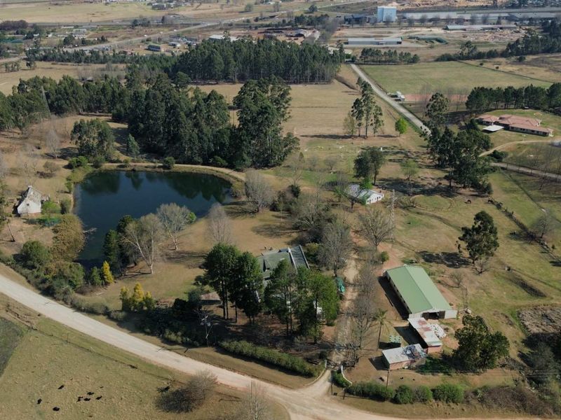 Aerial view of a rural farm property featuring a private dam, multiple outbuildings, and extensive open land with established trees.
