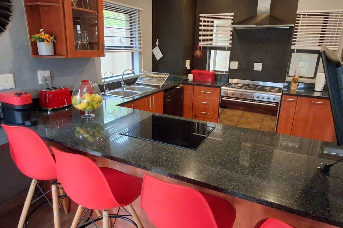 A functional kitchen featuring dark granite countertops, wooden cabinetry, a stainless steel gas stove with extractor fan, and a double basin sink.