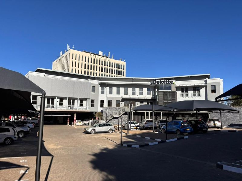 Exterior view of a modern multi-story office building featuring a paved parking area with shade cloth carports and visible balcony access.