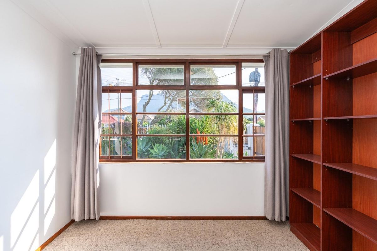 A bright, empty bedroom featuring a large timber-framed window with garden views and a built-in wooden shelving unit.