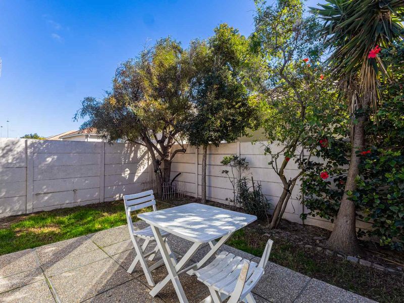 A private rear garden area featuring a paved patio space enclosed by a precast concrete boundary wall and established trees.