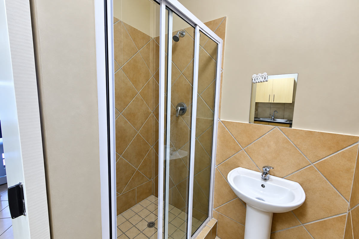 A functional bathroom featuring a tiled shower enclosure, a pedestal basin, and neutral wall finishes, presenting a clean and well-maintained space.