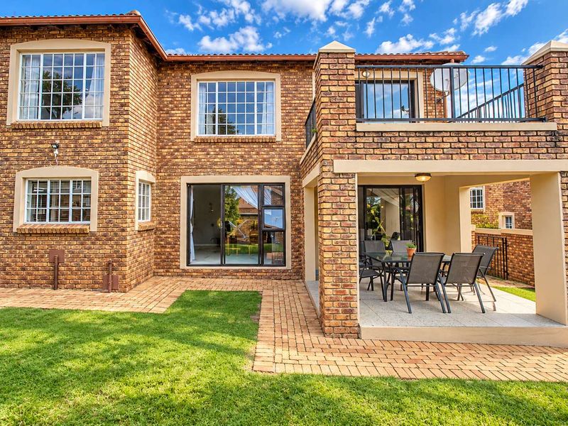 Rear view of a double-story townhouse featuring face brick construction, a covered patio, an upper-level balcony with metal railings, and a paved garden area.