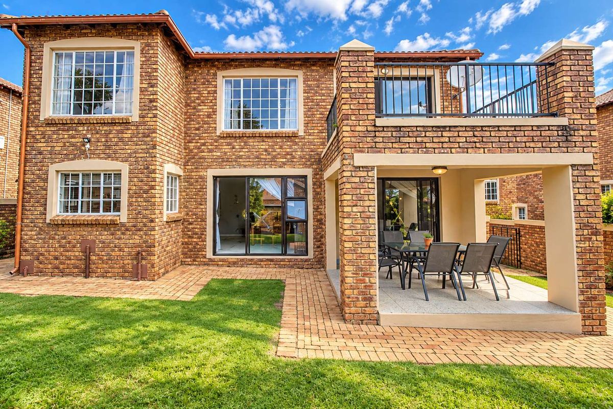 Rear view of a double-story townhouse featuring face brick construction, a covered patio, an upper-level balcony with metal railings, and a paved garden area.