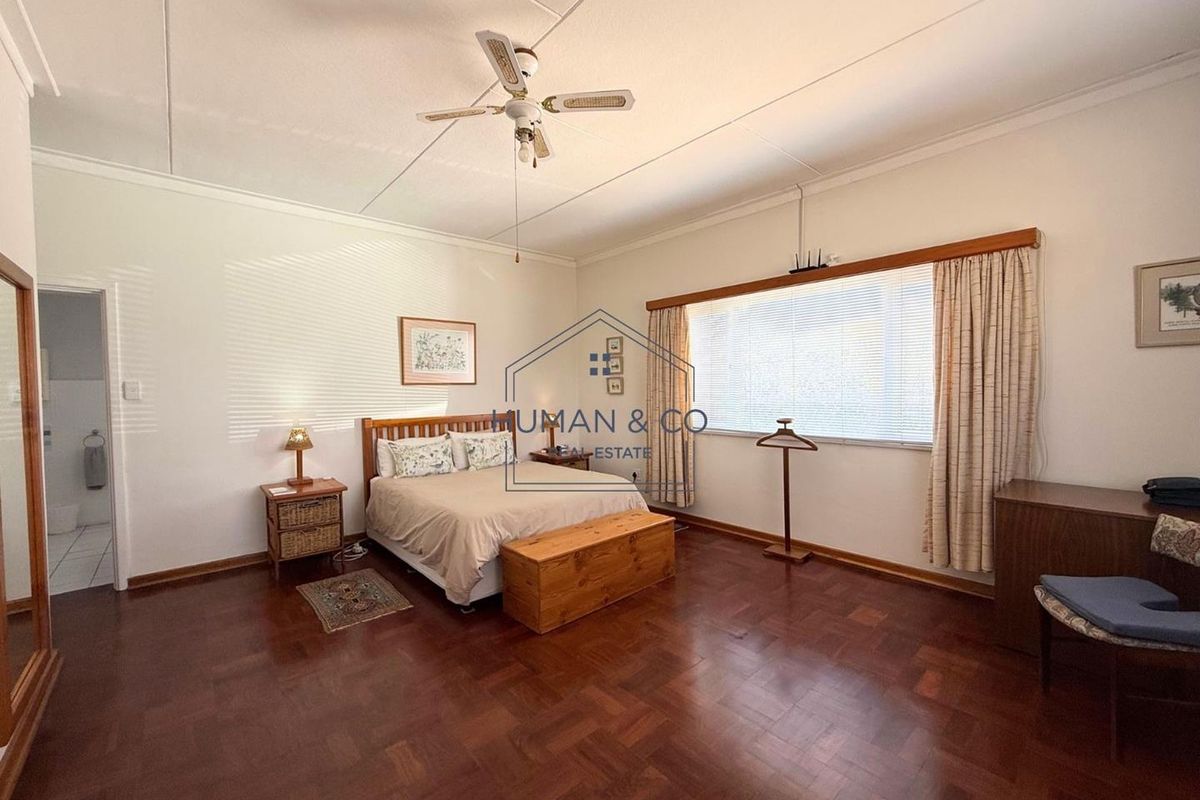 Spacious bedroom featuring polished parquet flooring, a ceiling fan, and large windows allowing for natural light.