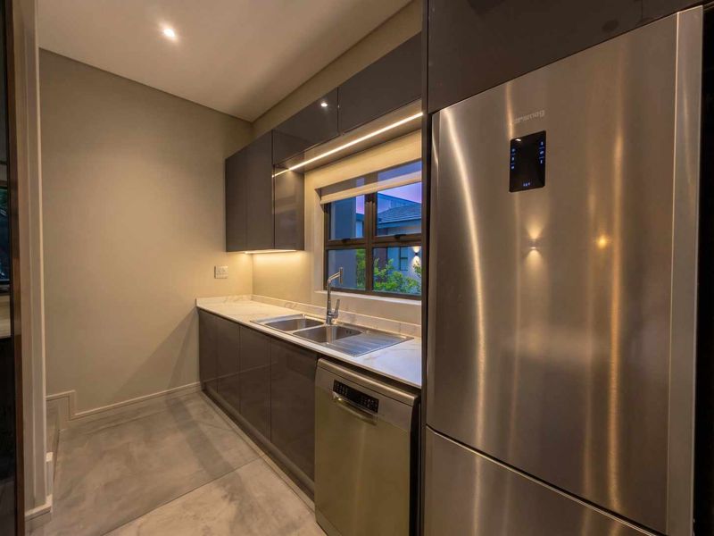 Modern kitchen featuring sleek grey cabinetry, stone countertops, integrated appliances, and under-cabinet lighting, creating a clean and functional workspace.