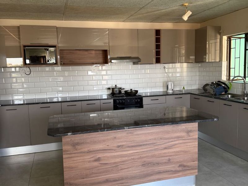 Modern kitchen featuring sleek cabinetry, a central island with stone countertop, subway tile backsplash, and integrated appliances.