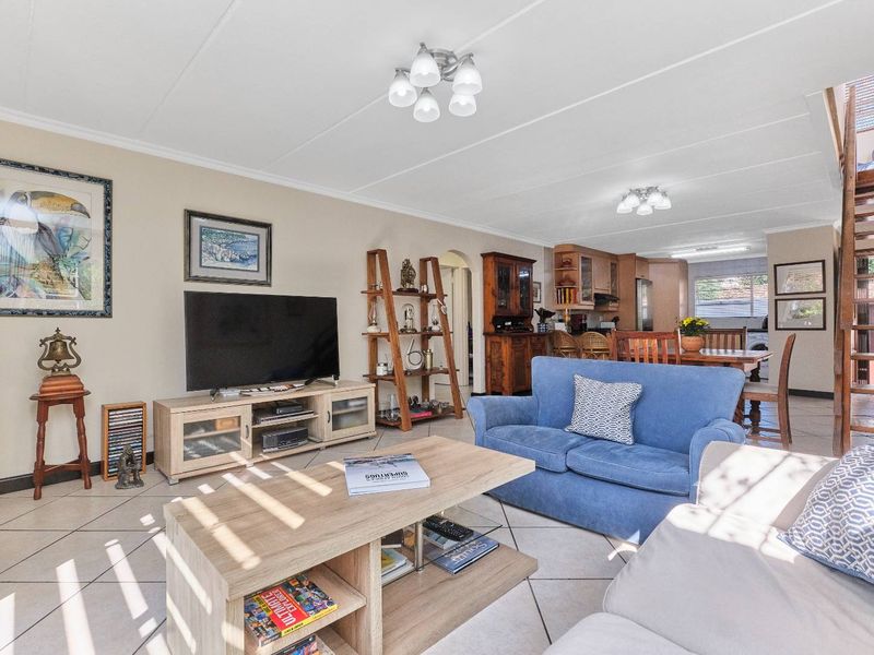 Spacious open-plan living and dining area featuring tiled flooring, neutral walls, and an integrated kitchen space with a staircase leading to the upper level.