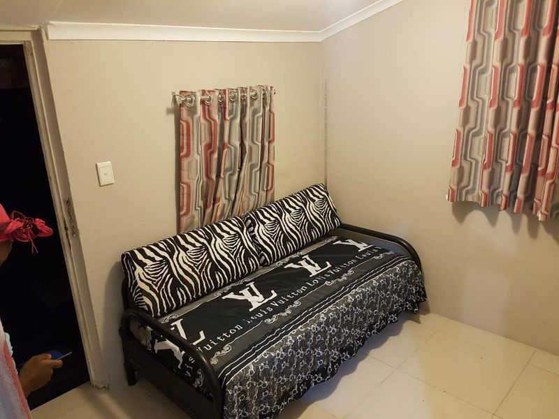 A compact bedroom featuring tiled flooring and coved ceiling details, currently used as a guest or secondary sleeping space.