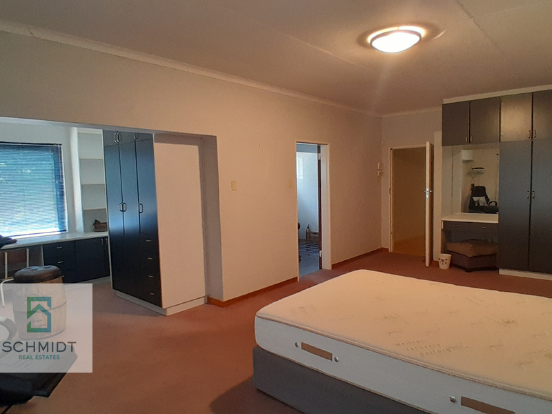 Spacious bedroom featuring extensive built-in cabinetry, a dedicated desk area, and carpeted flooring, offering ample storage and functional living space.