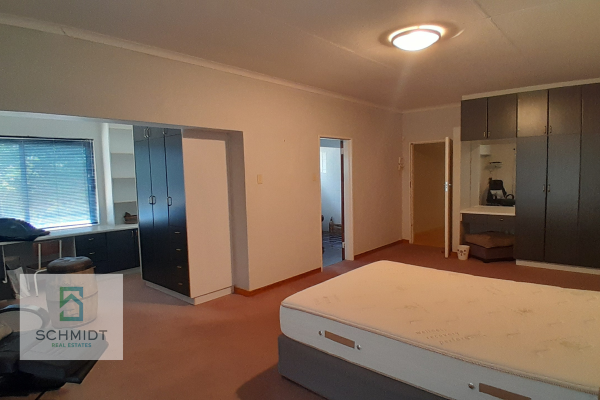 Spacious bedroom featuring extensive built-in cabinetry, a dedicated desk area, and carpeted flooring, offering ample storage and functional living space.
