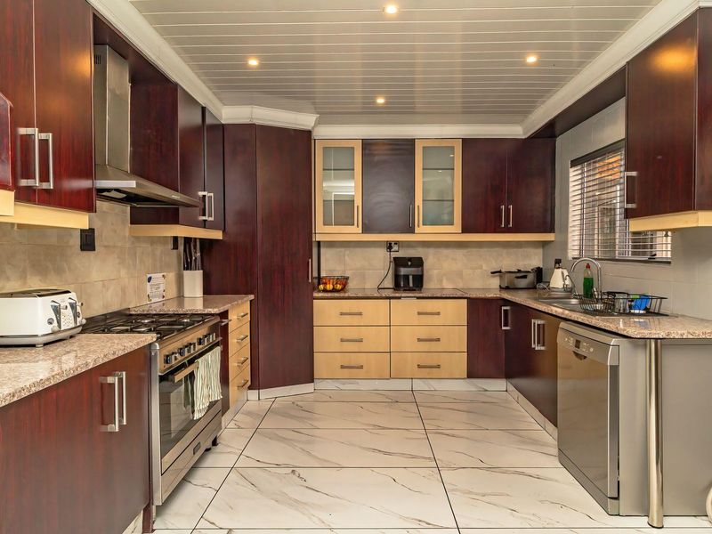 A well-appointed kitchen featuring dark wood cabinetry, granite countertops, gas hob, integrated appliances, and modern marble-look floor tiles.
