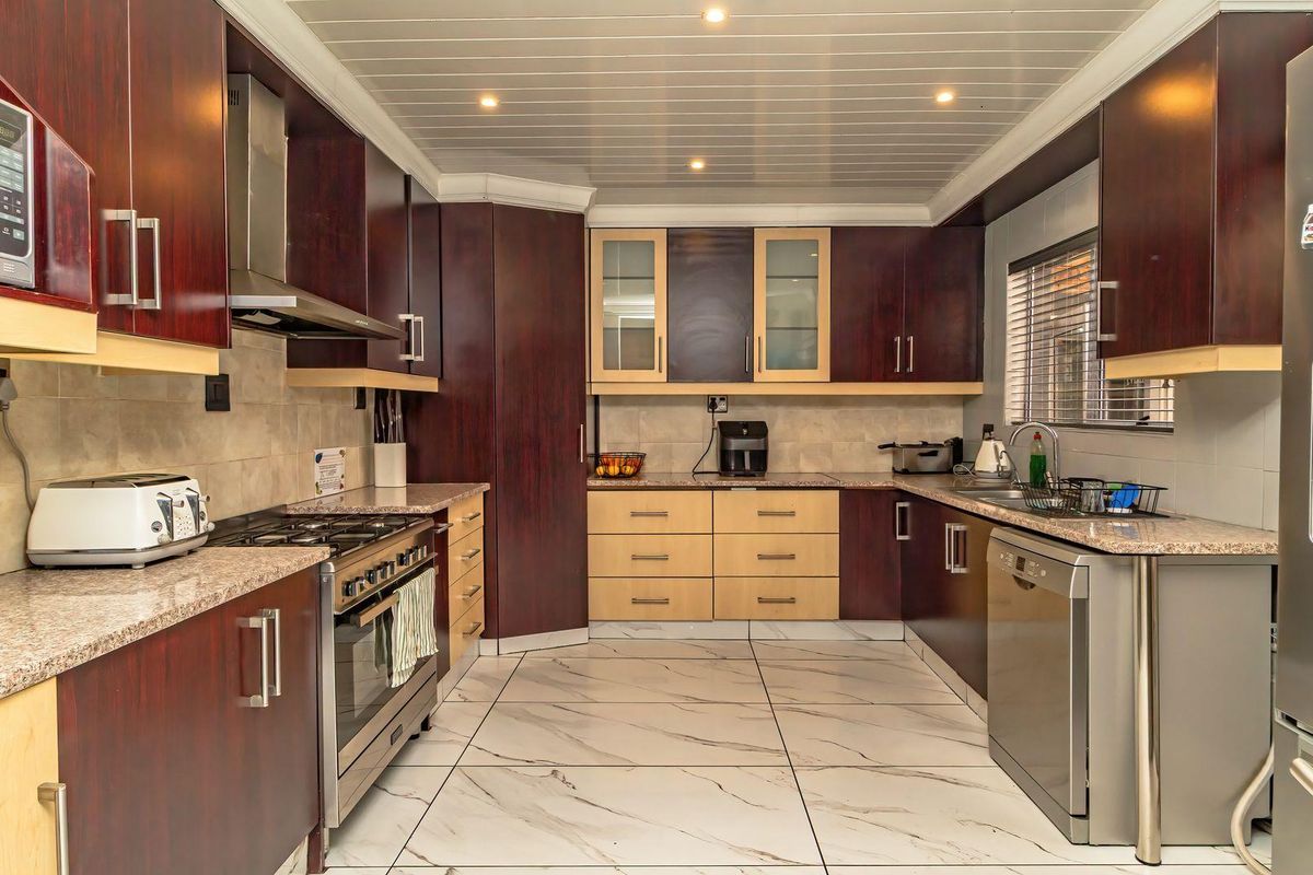 A well-appointed kitchen featuring dark wood cabinetry, granite countertops, gas hob, integrated appliances, and modern marble-look floor tiles.
